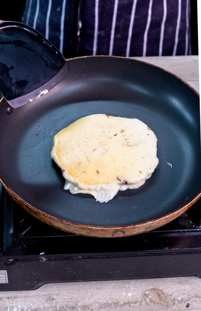 Golden Oreo pancake cooking in skillet with spatula