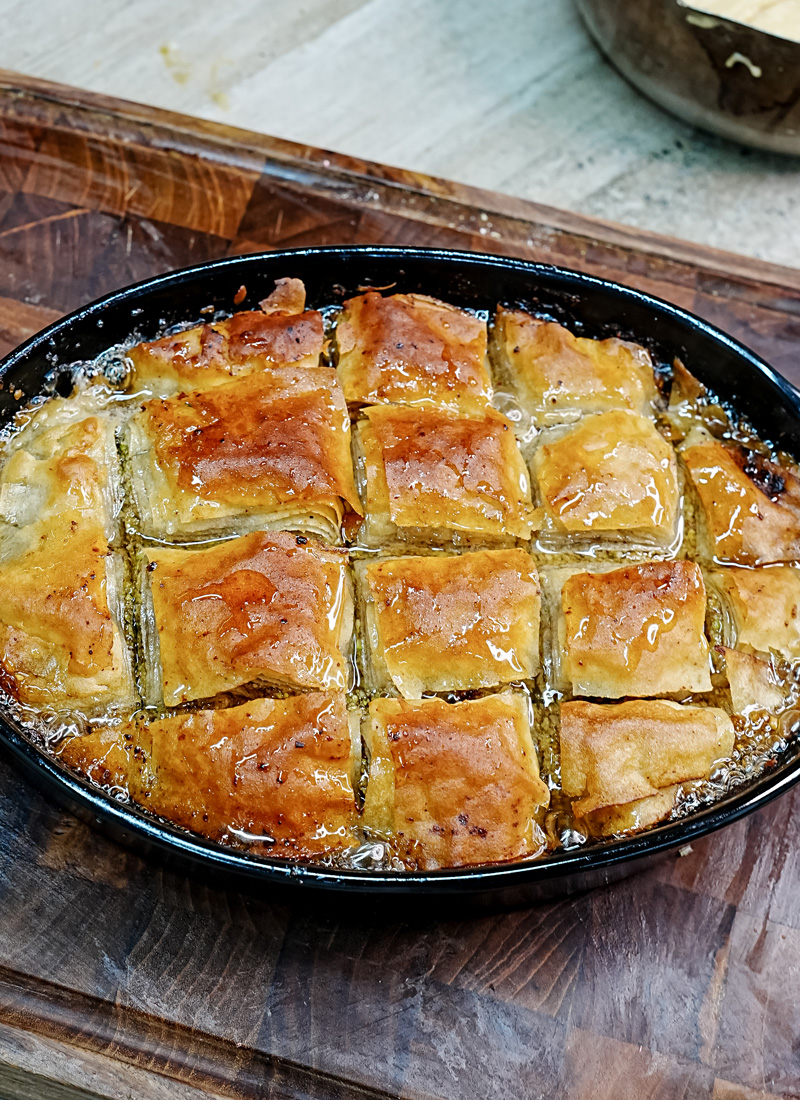 Golden baked baklava pieces with syrup in pan