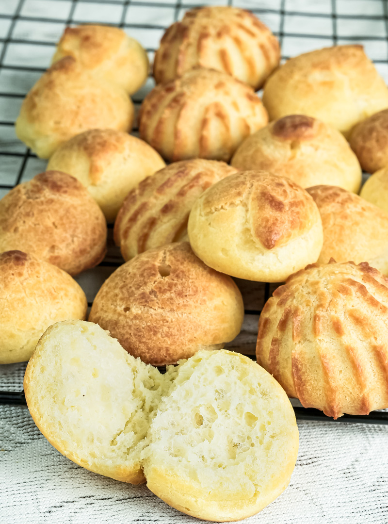 Golden baked choux pastry on cooling rack with one cut open showing hollow interior