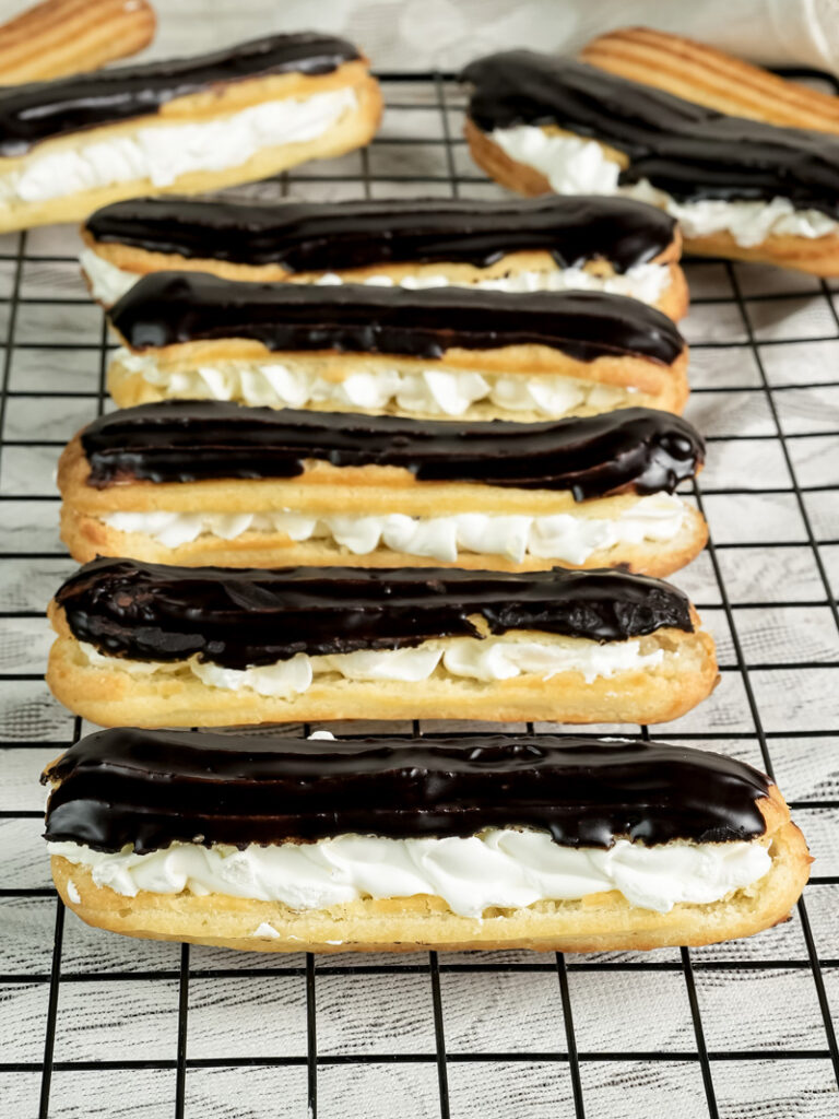 Golden baked eclairs with chocolate glaze and cream filling on wire rack