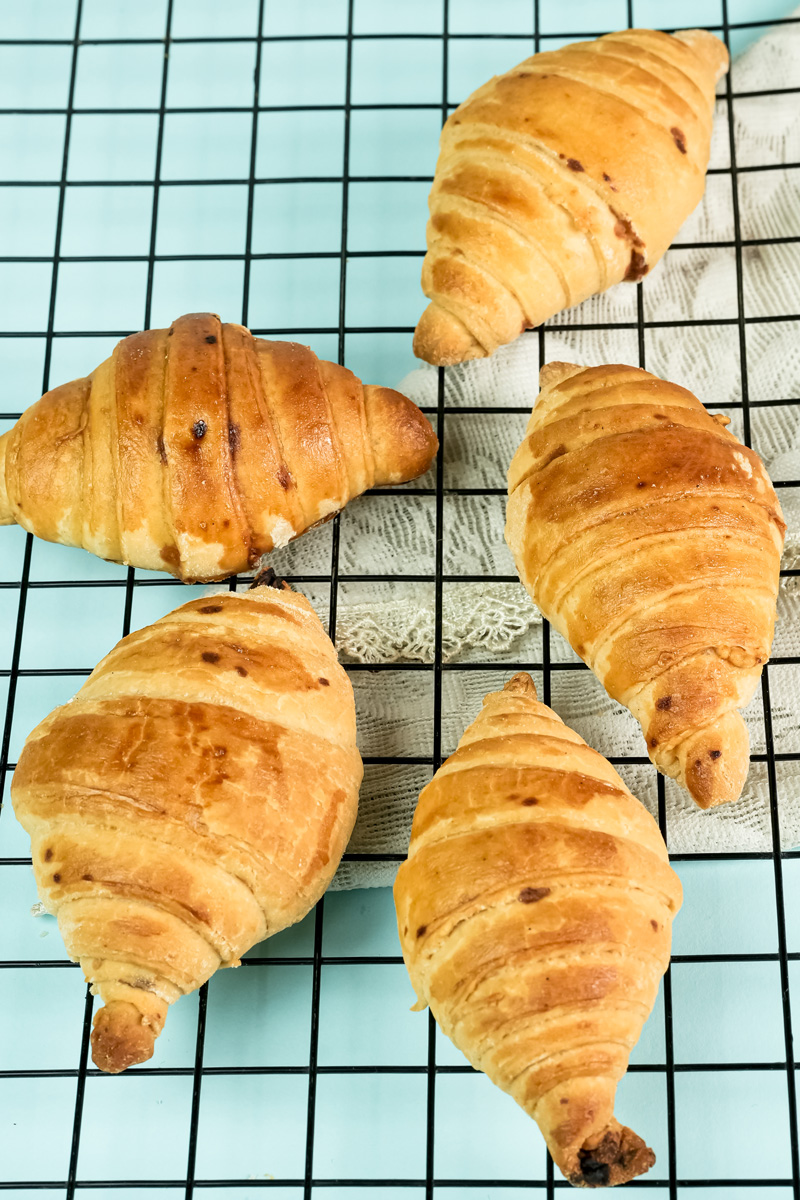 Golden brown baked croissants cooling on wire rack