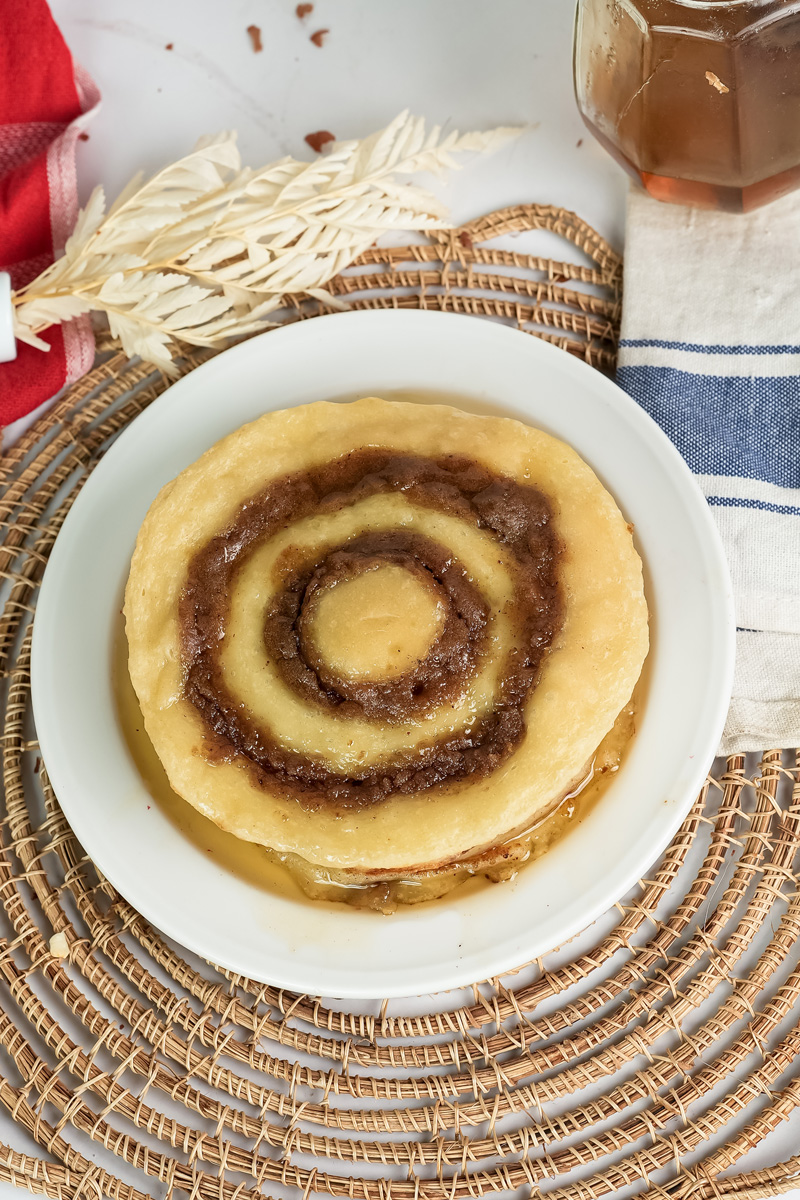 Golden cinnamon roll pancake with caramel spiral on white plate