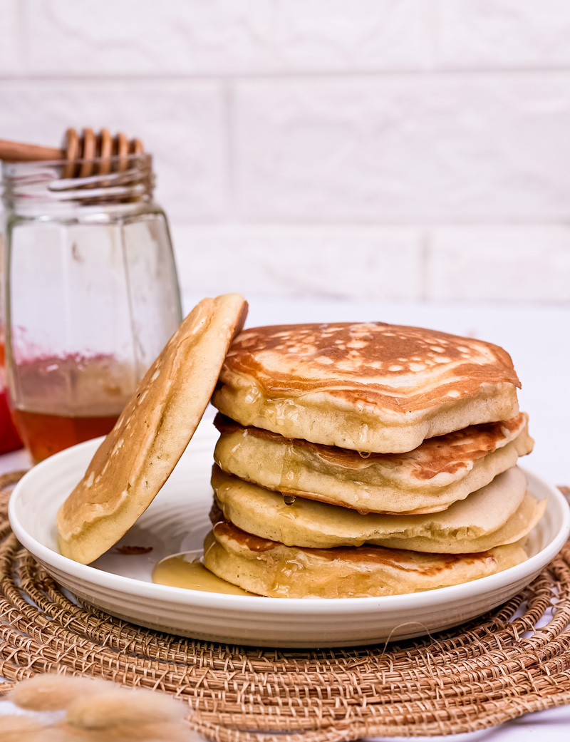Golden gluten free pancakes stacked on white plate with honey jar