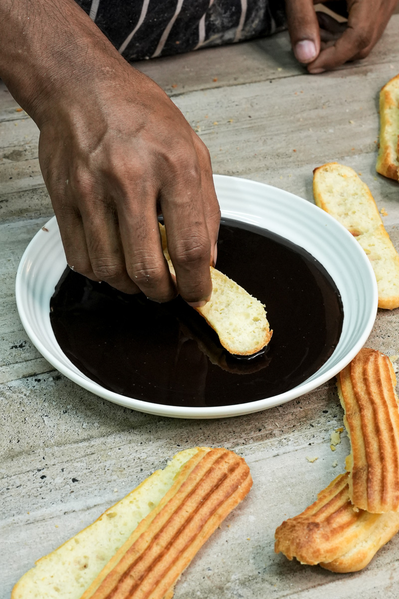 Hand dipping eclair shell into dark chocolate glaze for homemade pastry recipe