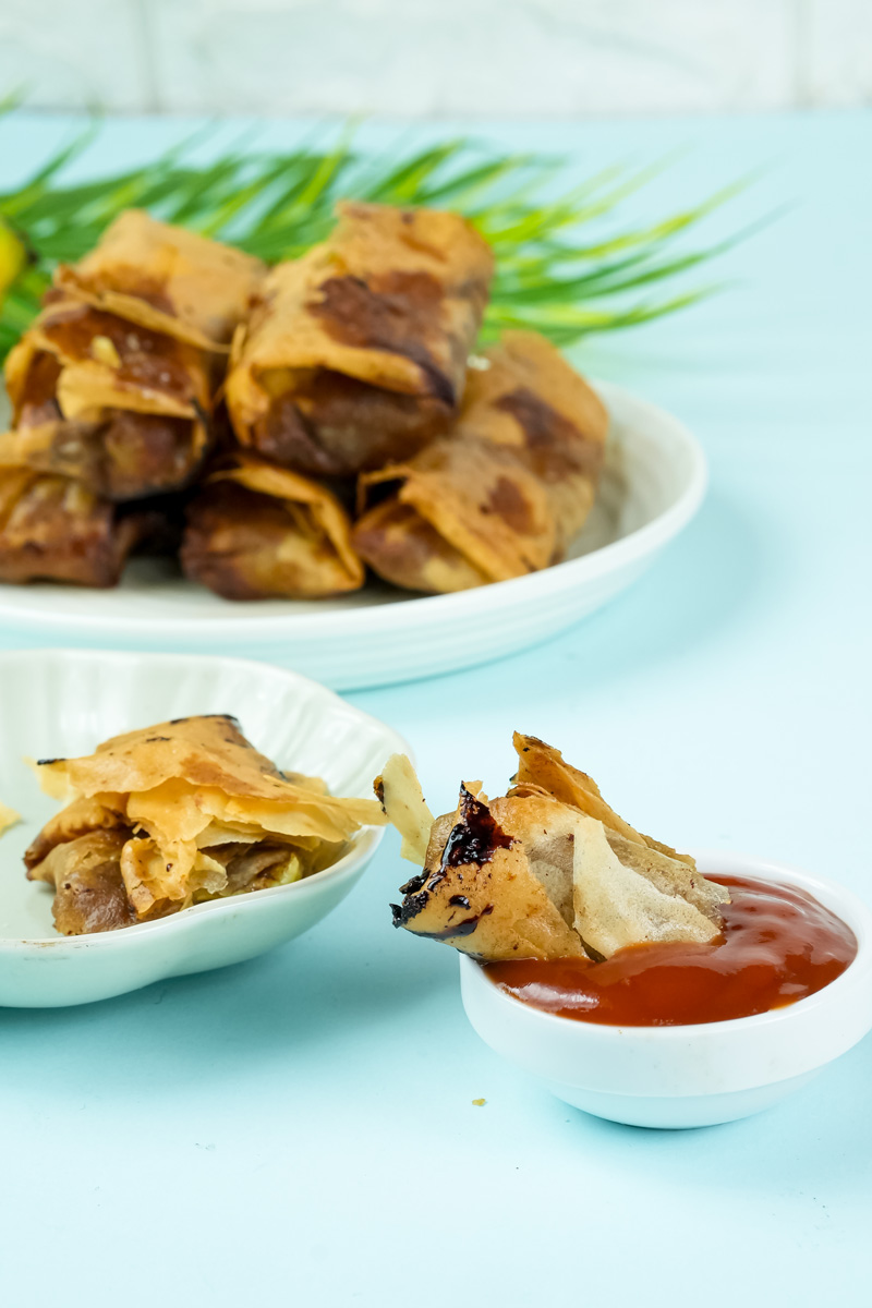 Hand holding banana lumpia with sauce