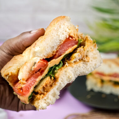 Hand holding bite of focaccia sandwich with tomato and greens