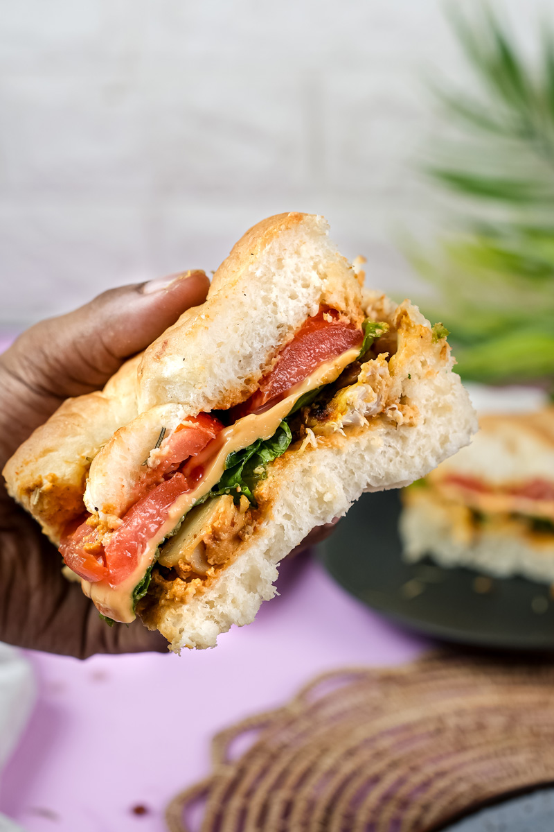 Hand holding bite of focaccia sandwich with tomato and greens