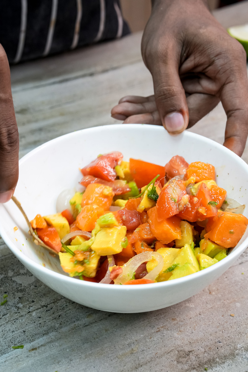 Hands mixing fresh mango avocado salad ingredients
