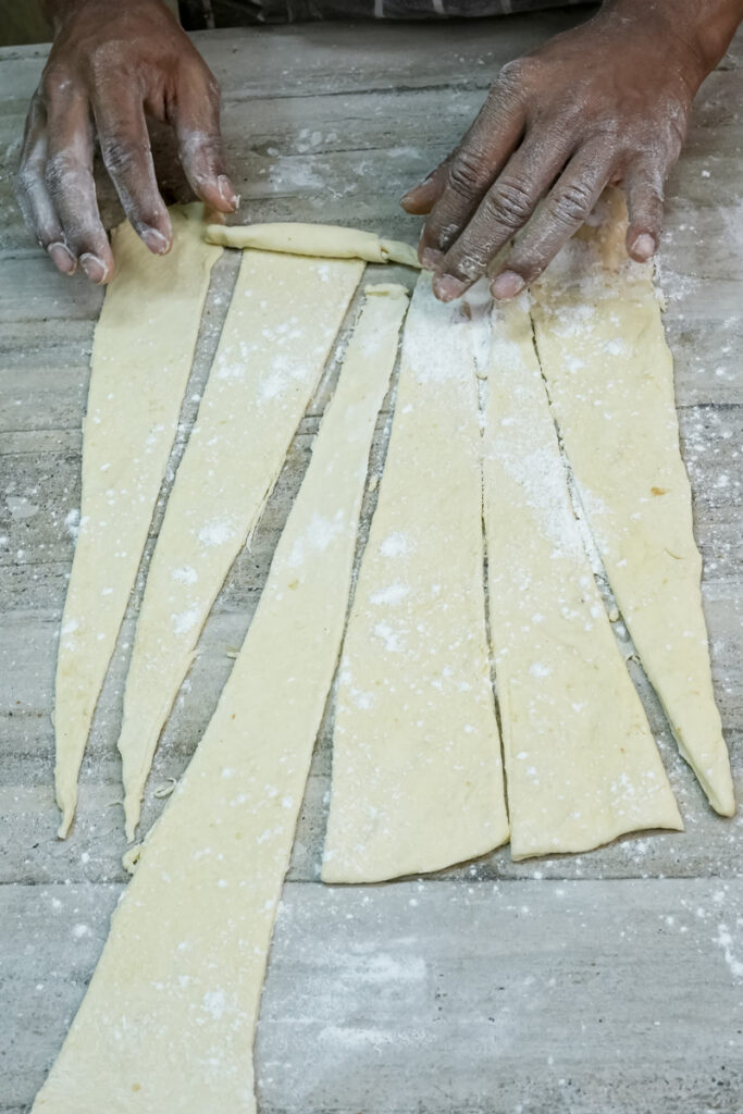 Hands rolling croissant dough strips into crescent shape