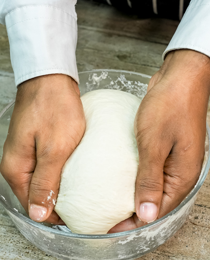 Hands shaping focaccia dough in bowl