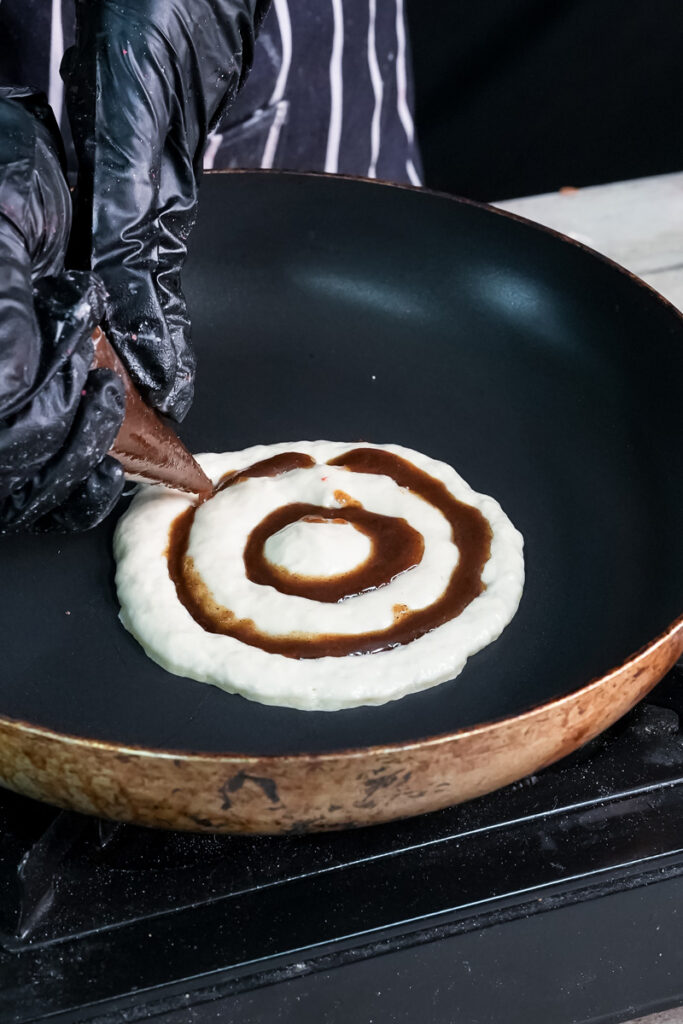Homemade cinnamon roll pancake batter with cinnamon swirl in non-stick pan