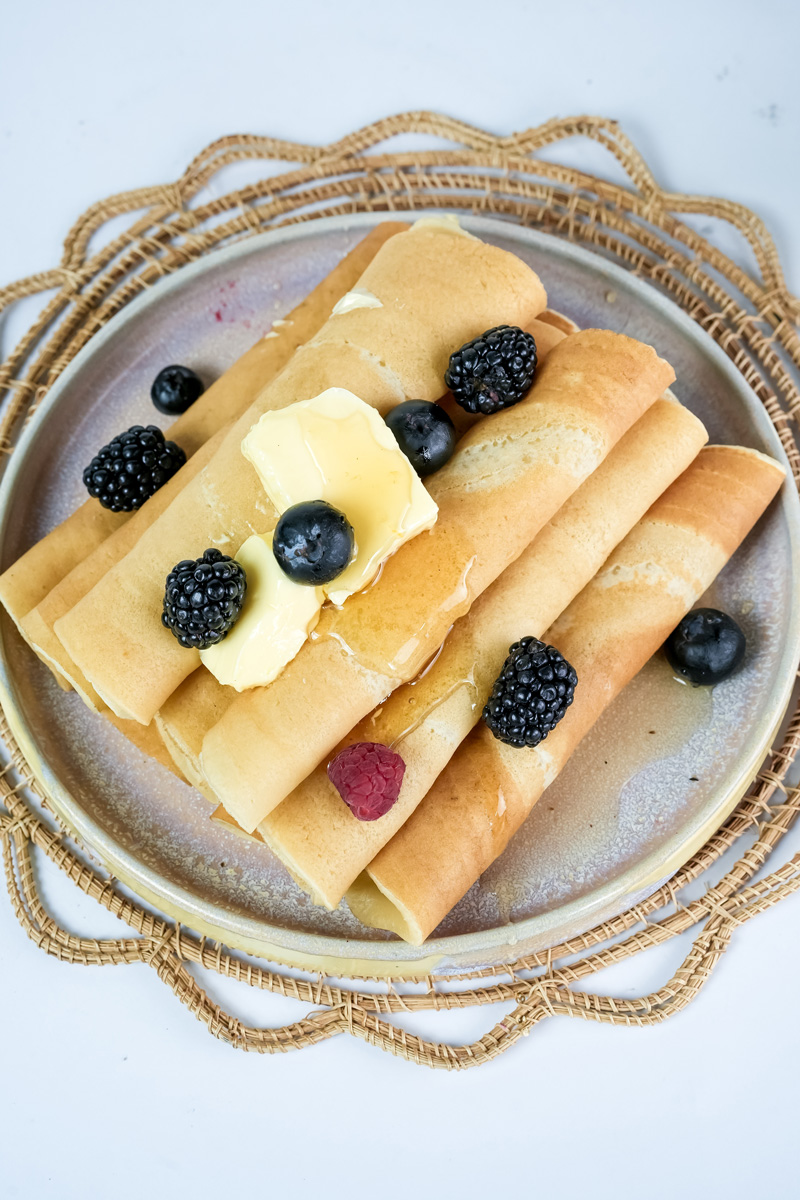 Homemade pancake rolls with fresh berries and butter on decorative plate