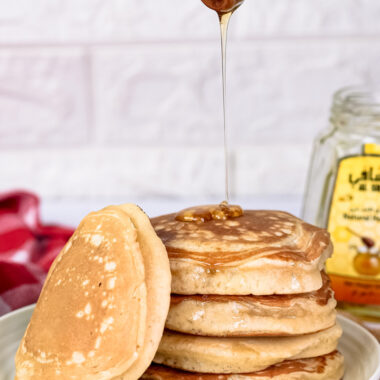 Honey being drizzled onto stack of gluten free pancakes with wooden dipper