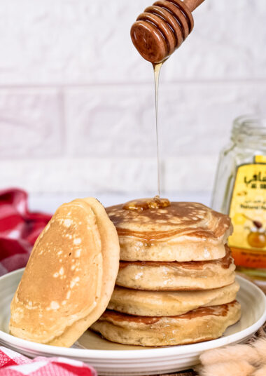 Honey being drizzled onto stack of gluten free pancakes with wooden dipper