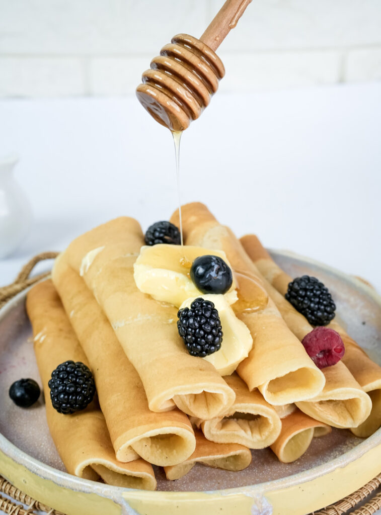 Honey being drizzled over pancake rolls with fresh berry toppings