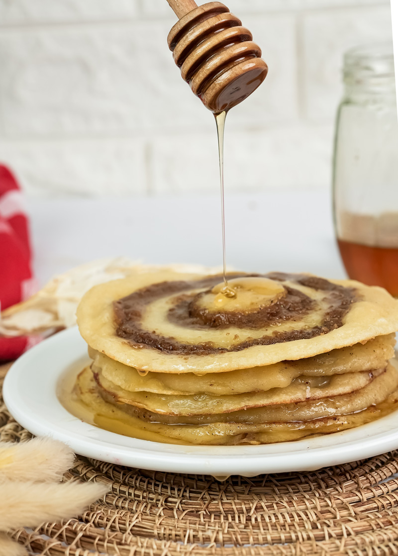 Honey drizzling over cinnamon roll pancake stack with wooden honey dipper