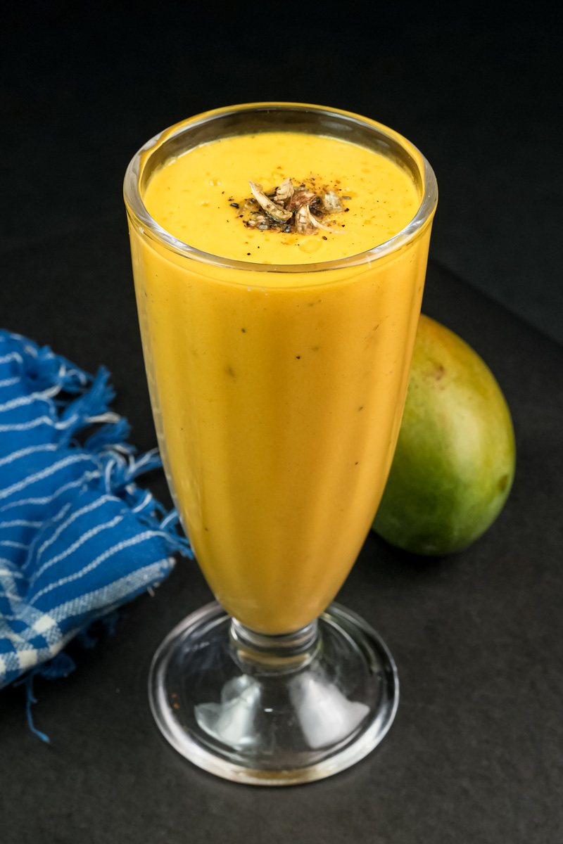 Mango lassi with fresh mango fruit in background