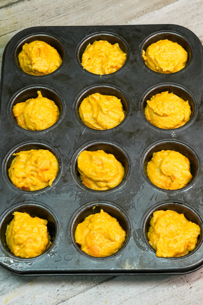 Muffin tin filled with mango muffin batter ready for baking