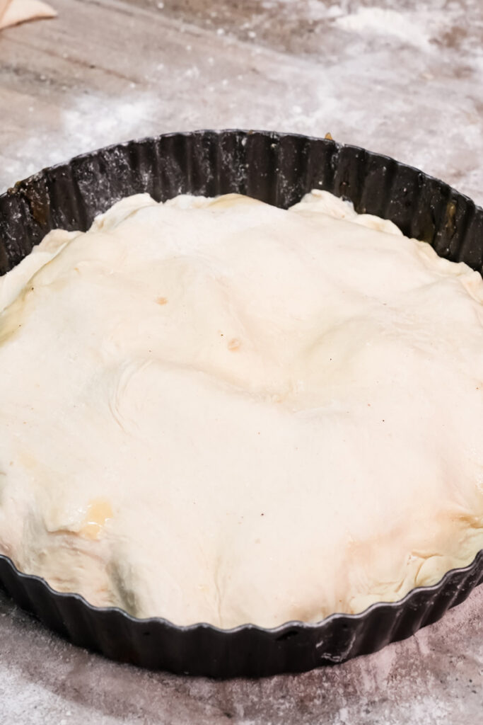 Pastry layer covering caramelized apples in Tarte Tatin pan