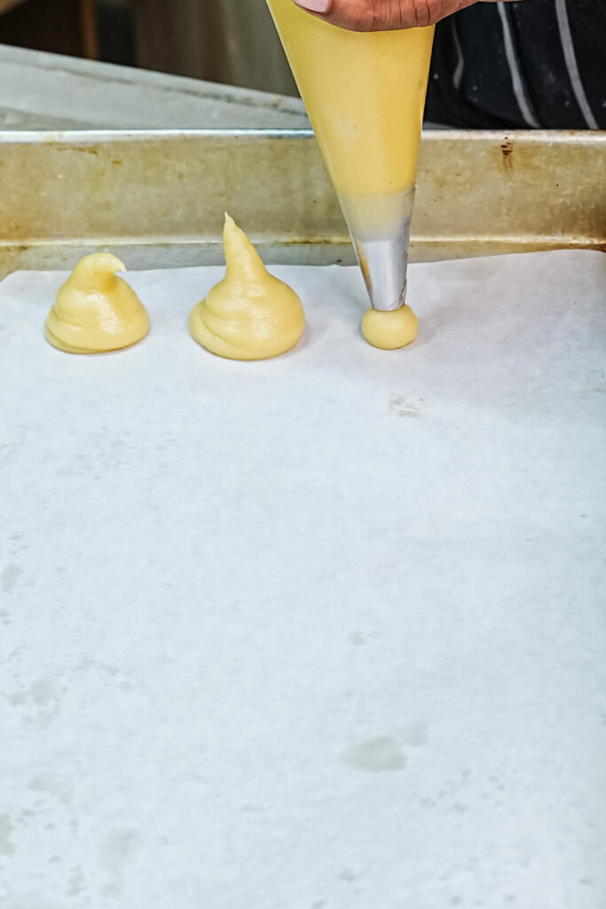 Piping choux pastry dough onto parchment-lined baking sheet