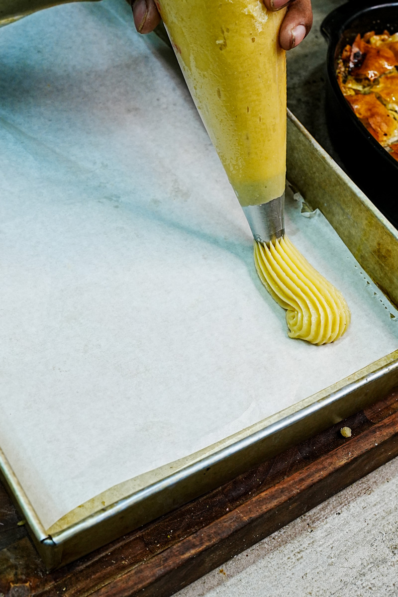 Piping choux pastry dough onto parchment-lined baking sheet for eclairs