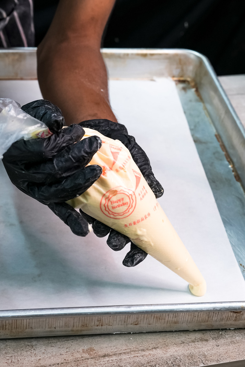 Piping ladyfinger batter onto parchment paper with pastry bag