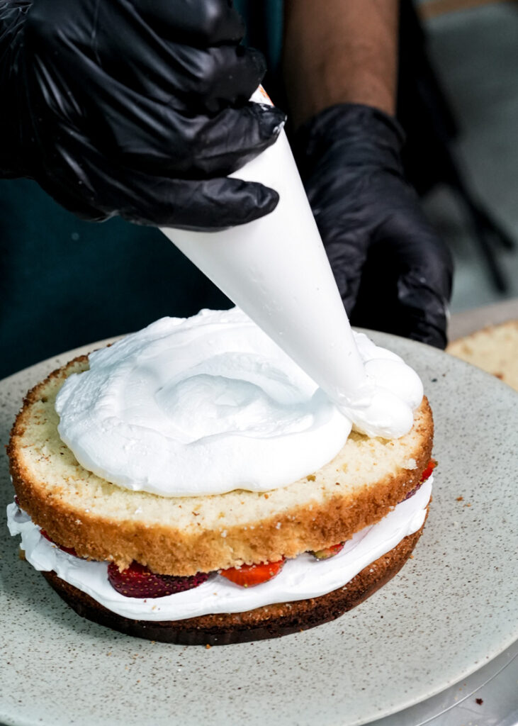 Piping whipped cream onto strawberry shortcake layer during assembly