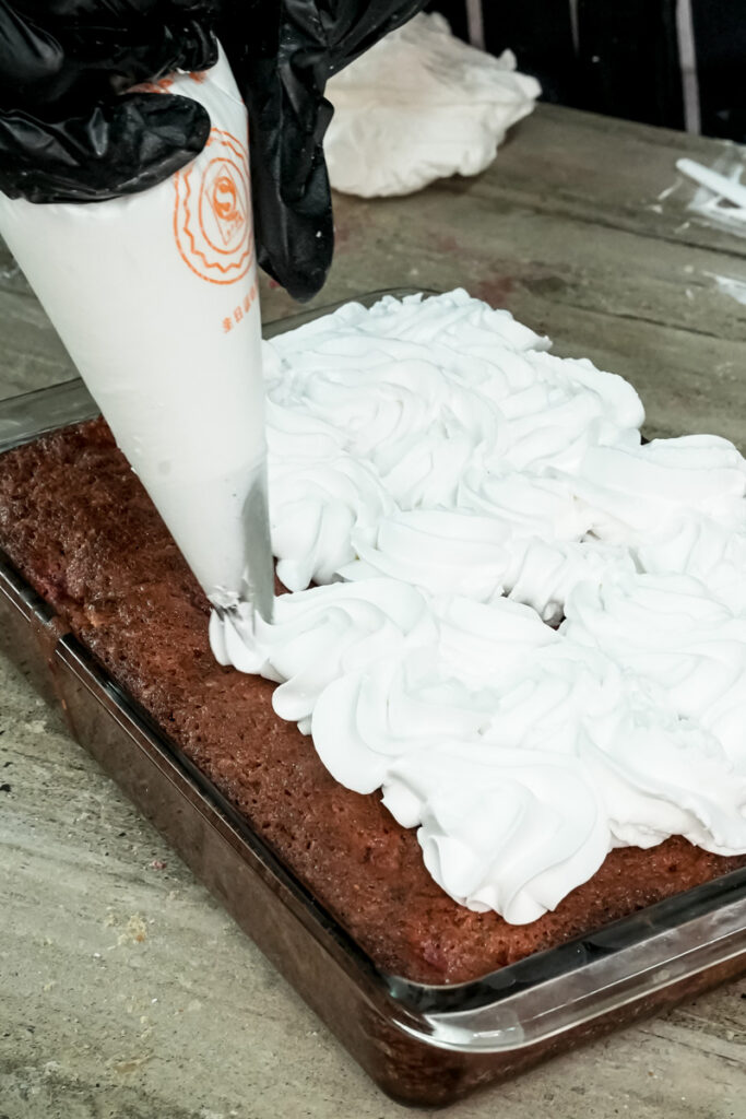 Piping white frosting onto baked strawberry earthquake cake