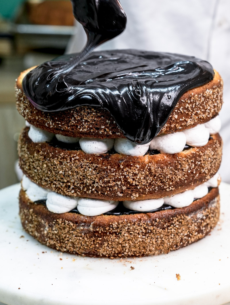 Pouring chocolate ganache drip over assembled churro layer cake
