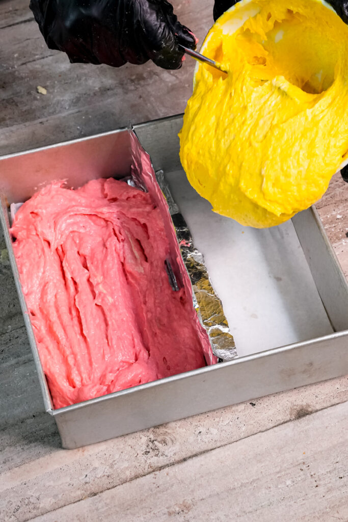 Pouring colored Battenberg batter into divided baking pan