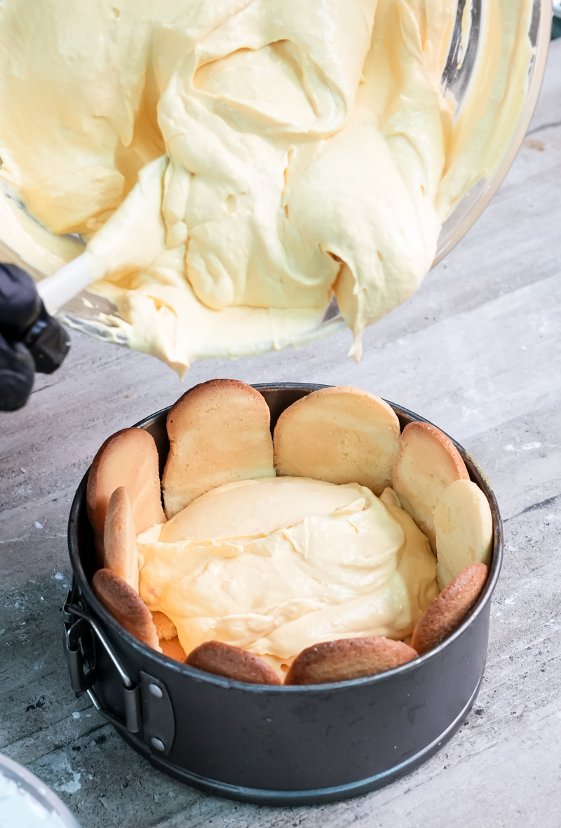 Pouring custard filling into ladyfinger-lined charlotte cake pan