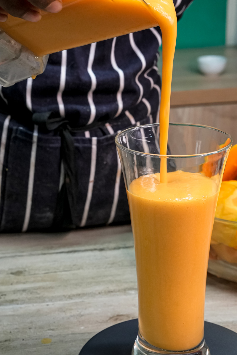 Pouring fresh mango milkshake into tall glass