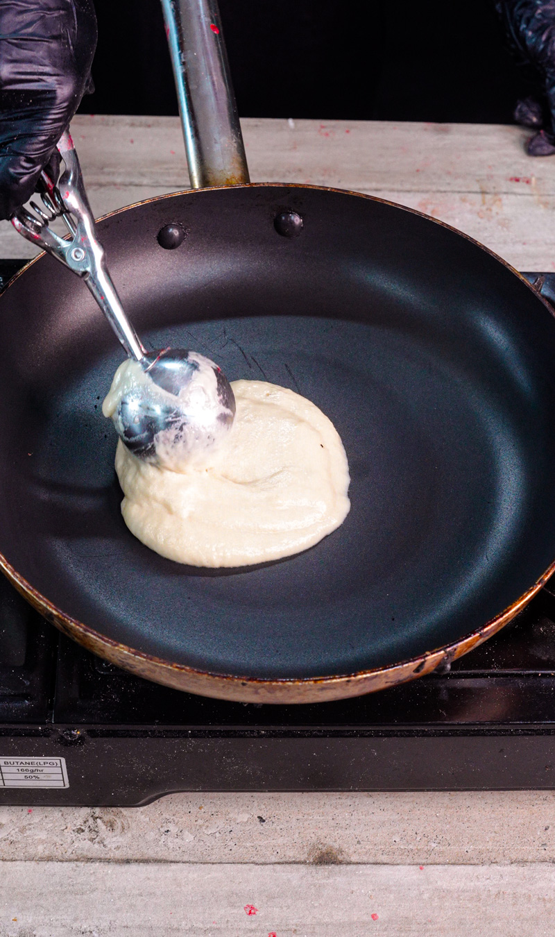 Pouring gluten free pancake batter into non-stick pan with ladle