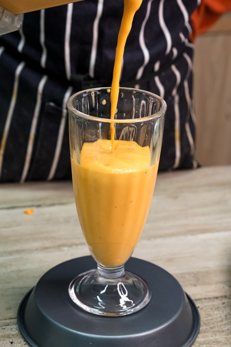 Pouring homemade mango lassi into tall glass