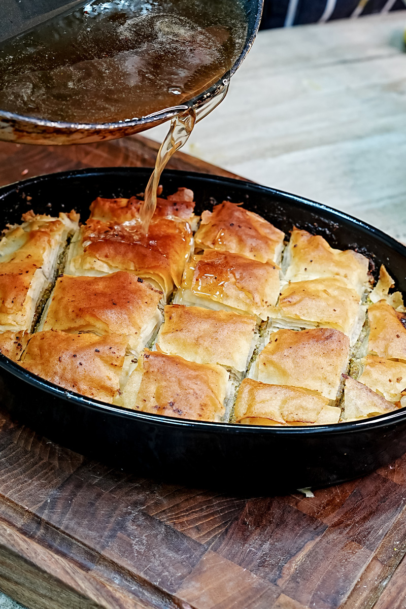 Pouring honey syrup over freshly baked baklava