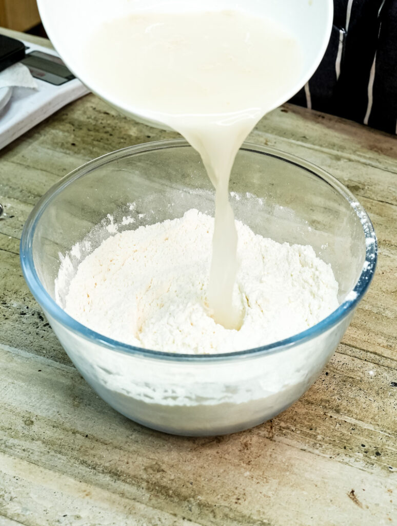 Pouring milk into flour for focaccia dough preparation