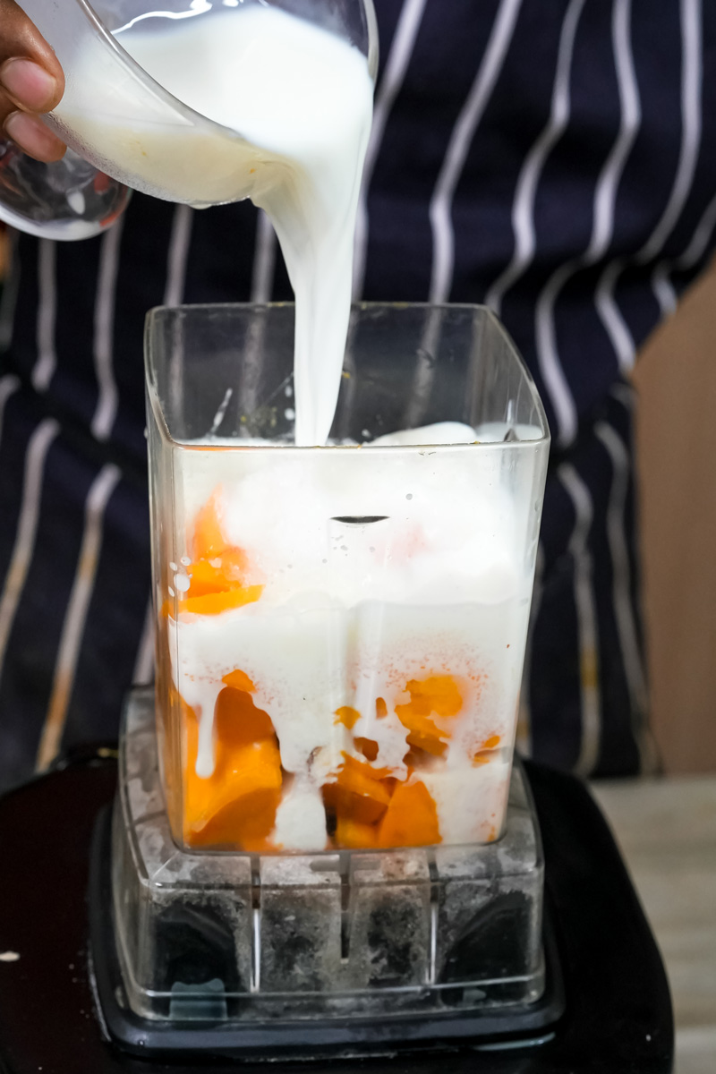 Pouring milk into mango lassi ingredients in blender