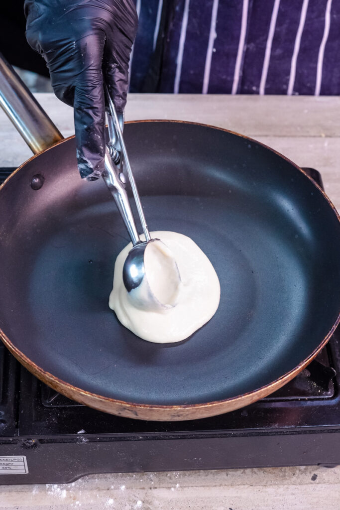 Pouring pancake roll batter into non-stick pan with ladle
