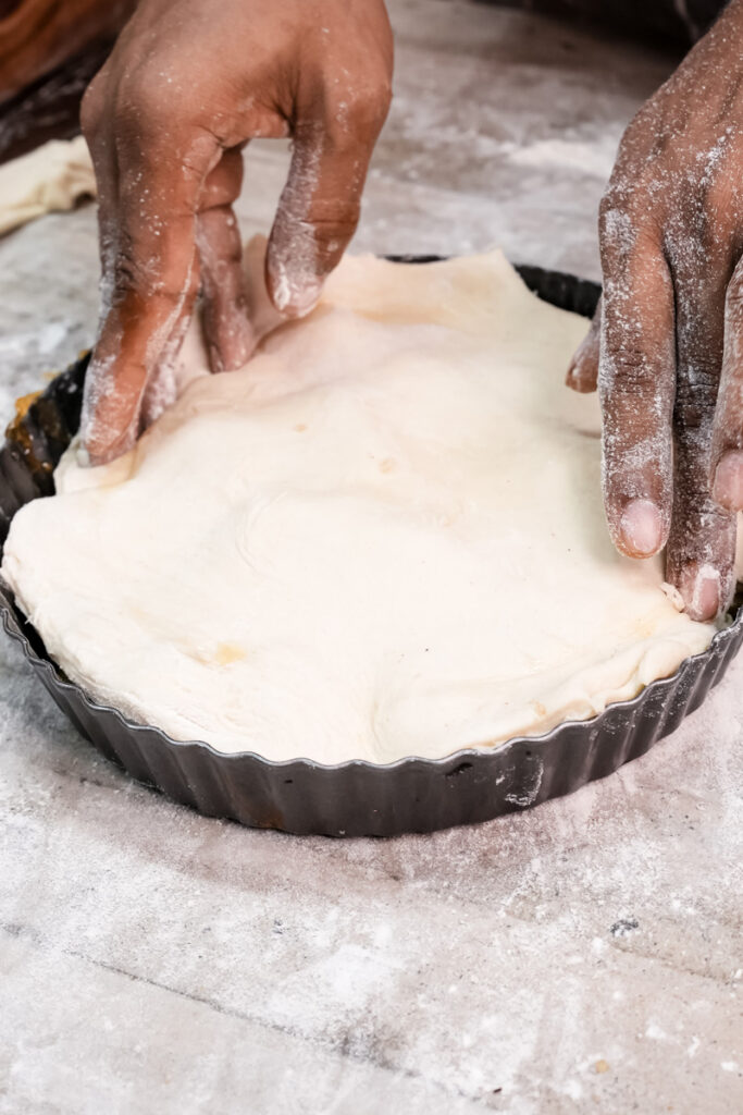 Pressing pastry dough over caramelized apples in tart pan