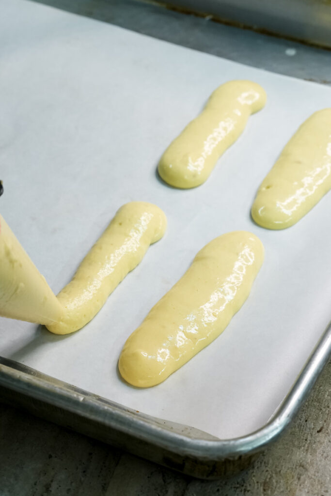 Raw ladyfinger cookies piped on baking sheet before baking