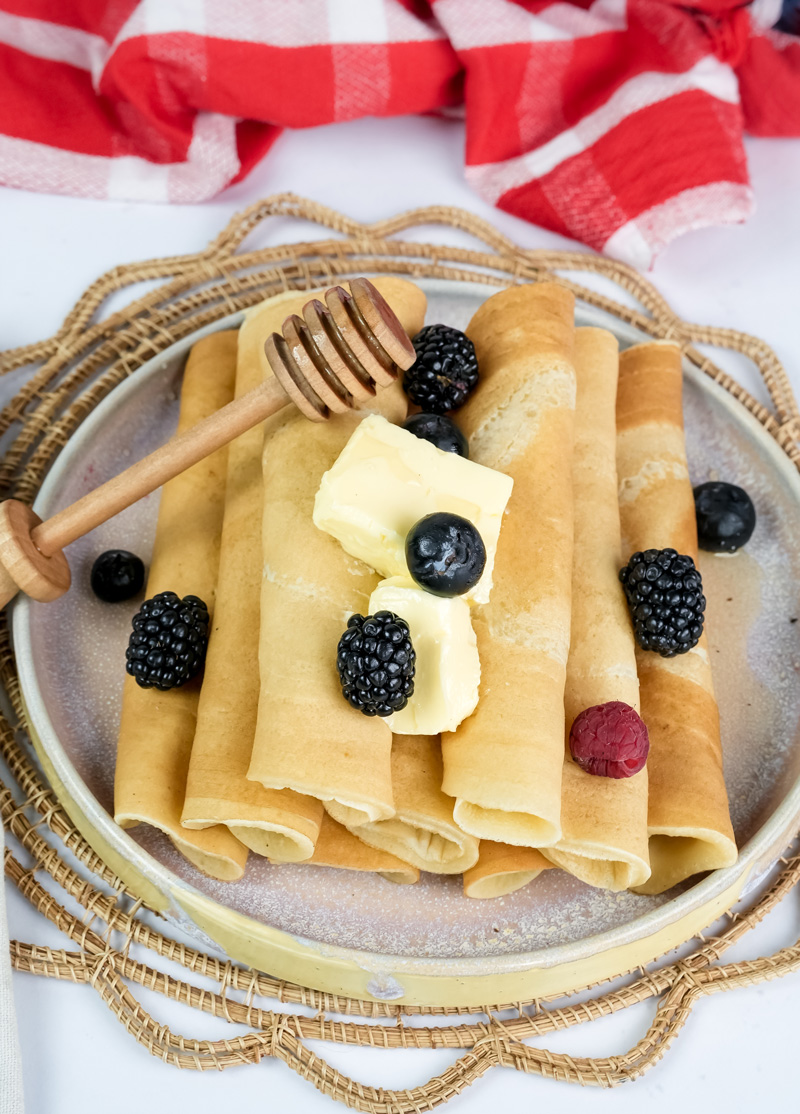 Rolled pancakes with mixed berries and butter cubes on rustic serving plate