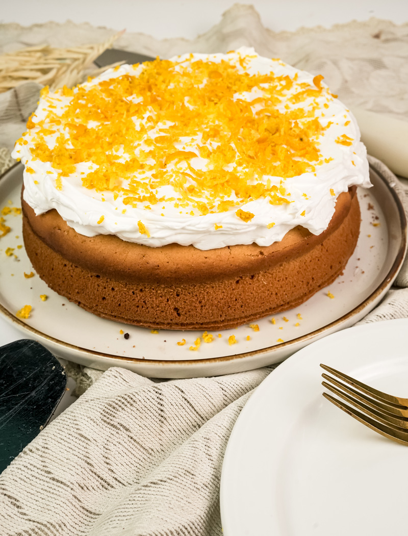 Round citrus cake decorated with whipped cream and orange zest