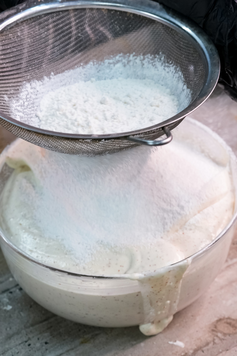 Sifting opera cake batter through fine mesh for smooth texture