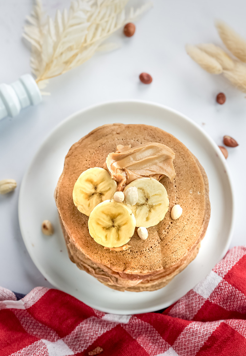 Single peanut butter pancake topped with banana slices and chopped nuts