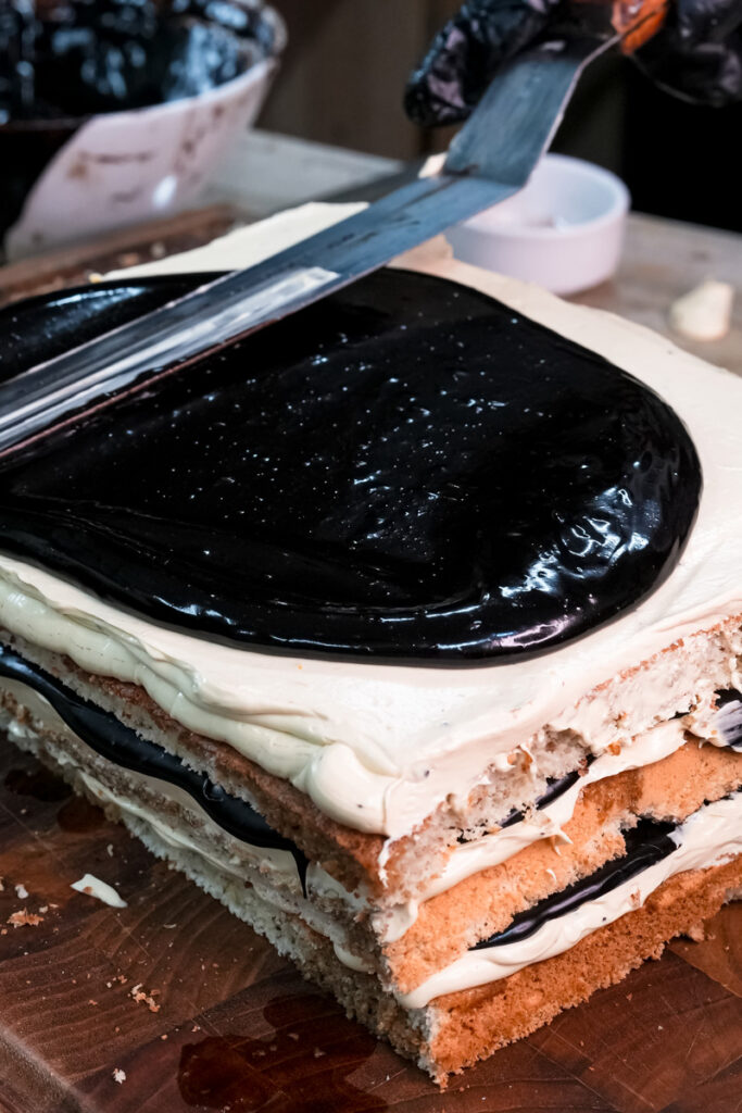 Piping white buttercream decoration on opera cake layers