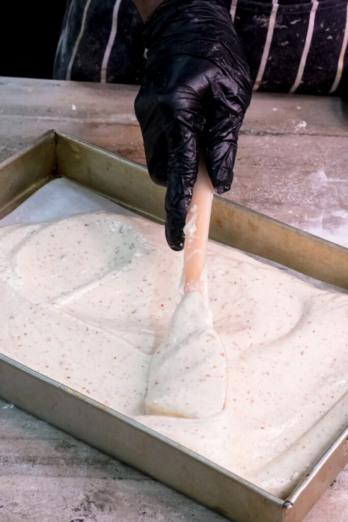 Smoothing opera cake batter evenly in baking pan with finger