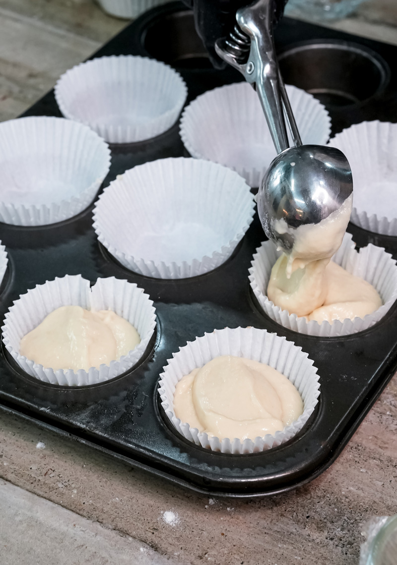 Spooning muffin batter into paper-lined muffin tin