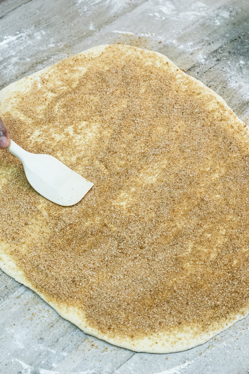 Spreading cinnamon filling evenly across dough with spatula