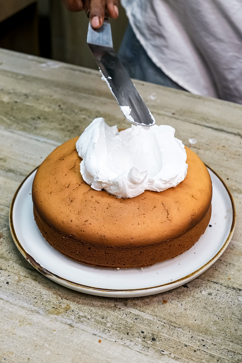 Spreading white frosting on citrus cake with knife