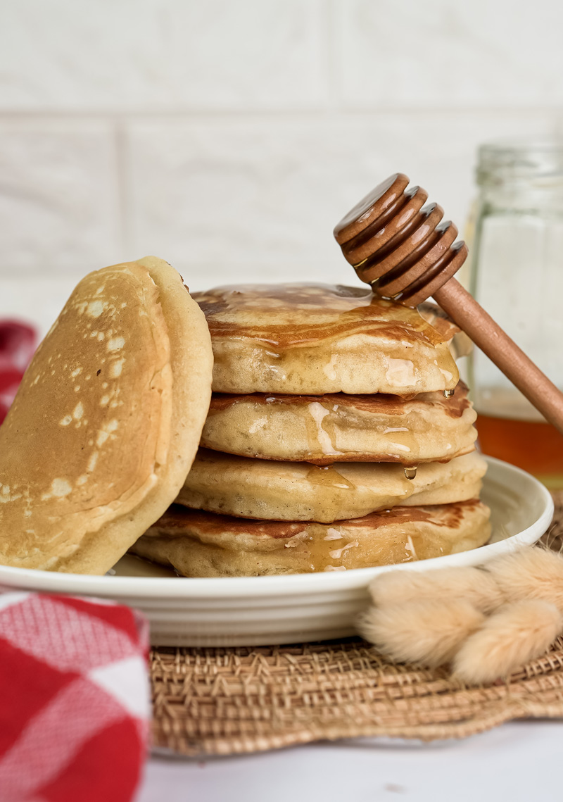 Stack of fluffy gluten free pancakes with honey drizzle and wooden honey dipper